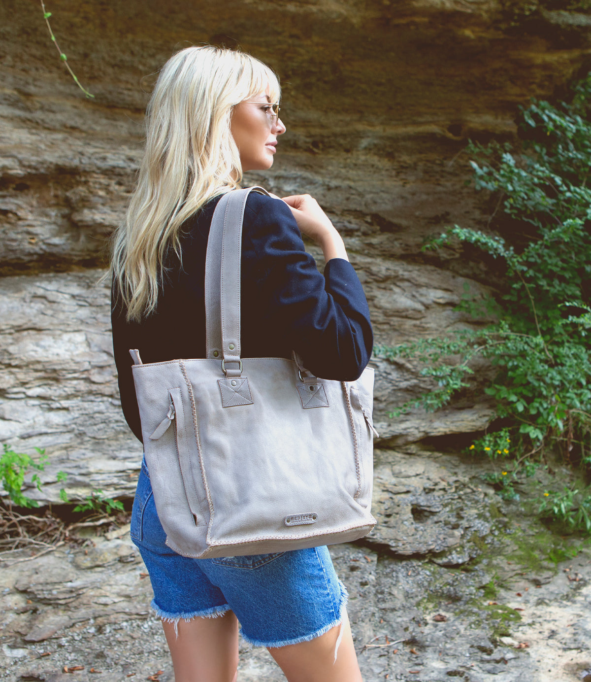 A woman, Bed Stu, is holding a beige tote bag.