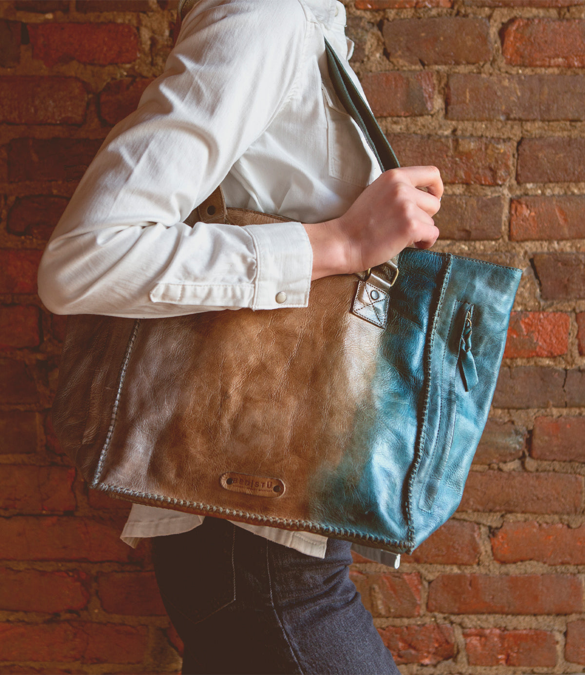 A woman holding a blue and brown zip-top tote bag, the Celindra LTC by Bed Stu.