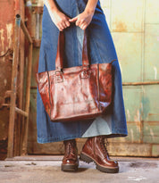 Bed Stu, a woman in a blue dress holding a brown tote bag, embarks on shopping adventures with her zip-top tote.