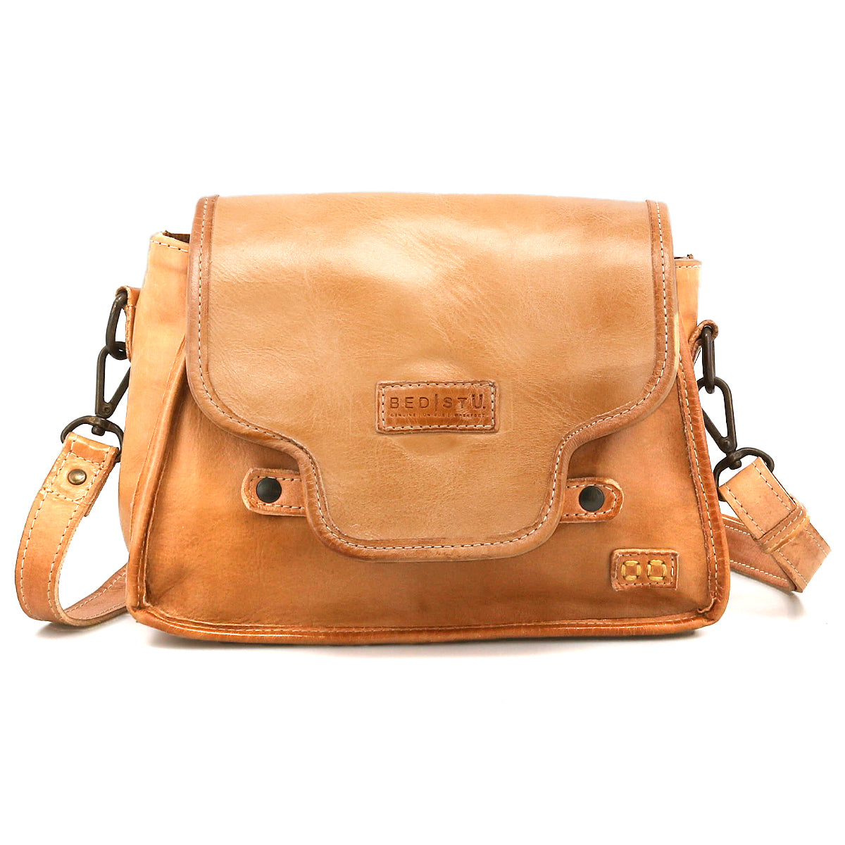 The Ceremonious by Bed Stu is a light brown leather flap-top bag featuring a front flap, magnetic closure, metal hardware, and an adjustable shoulder strap.