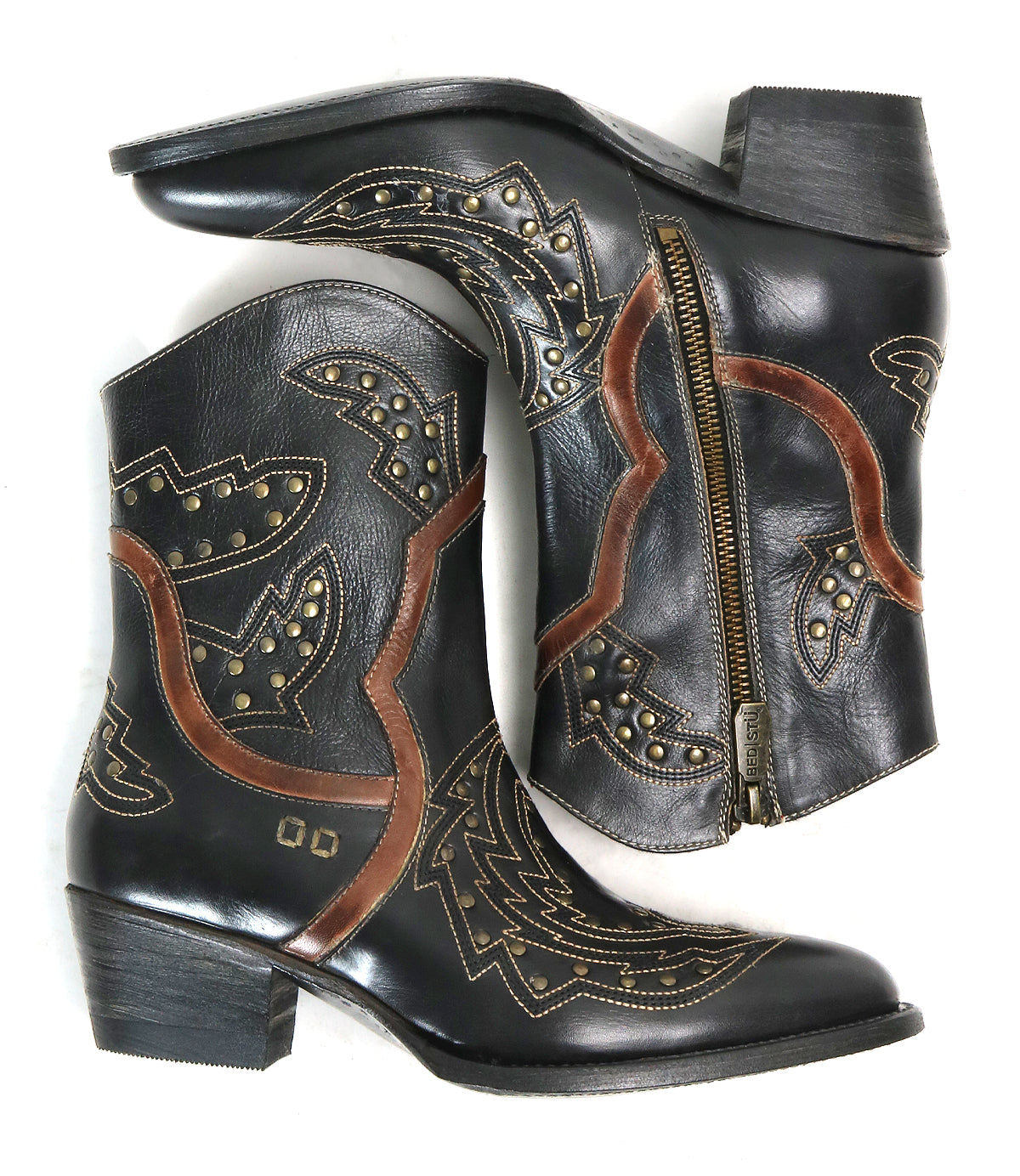 The Bed Stu Chamise boots—black leather western style with brown and tan stitching, stylish inlays, side zippers, snip toe, and stud accents—are shown arranged with one boot on its side and the other upright.