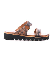 The Bed Stu Chow sandal features distressed brown leather, decorative metal accents, a cushioned tan footbed, and a chunky black platform sole with a wavy pattern.