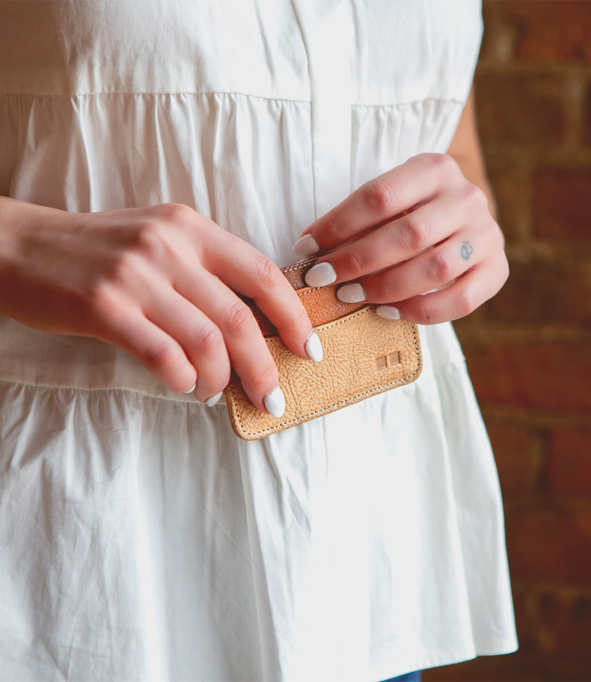 A woman in a white dress holding a Chuck by Bed Stu, a convenient small leather wallet.