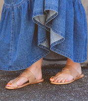 A person wearing a blue denim skirt and Bed Stu Civilized tan sandals with cushioned soles stands on a textured ground, exuding a laid-back style.
