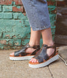 A woman wearing a pair of Bed Stu Clancy sandals with XL EXTRALIGHT soles standing in front of a brick wall.