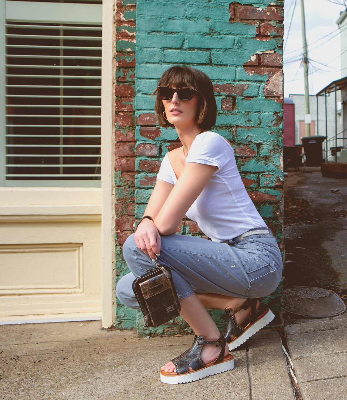 A woman crouching on the sidewalk, wearing Clancy shoes with a cushioned insole and a zip closure by Bed Stu.