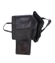 The Bed Stu Commuter is a black leather messenger bag with flap open, showing laptop compartments and a round brown patch on the inner flap, photographed on a white background—a sleek, multifunctional bag for commuters.