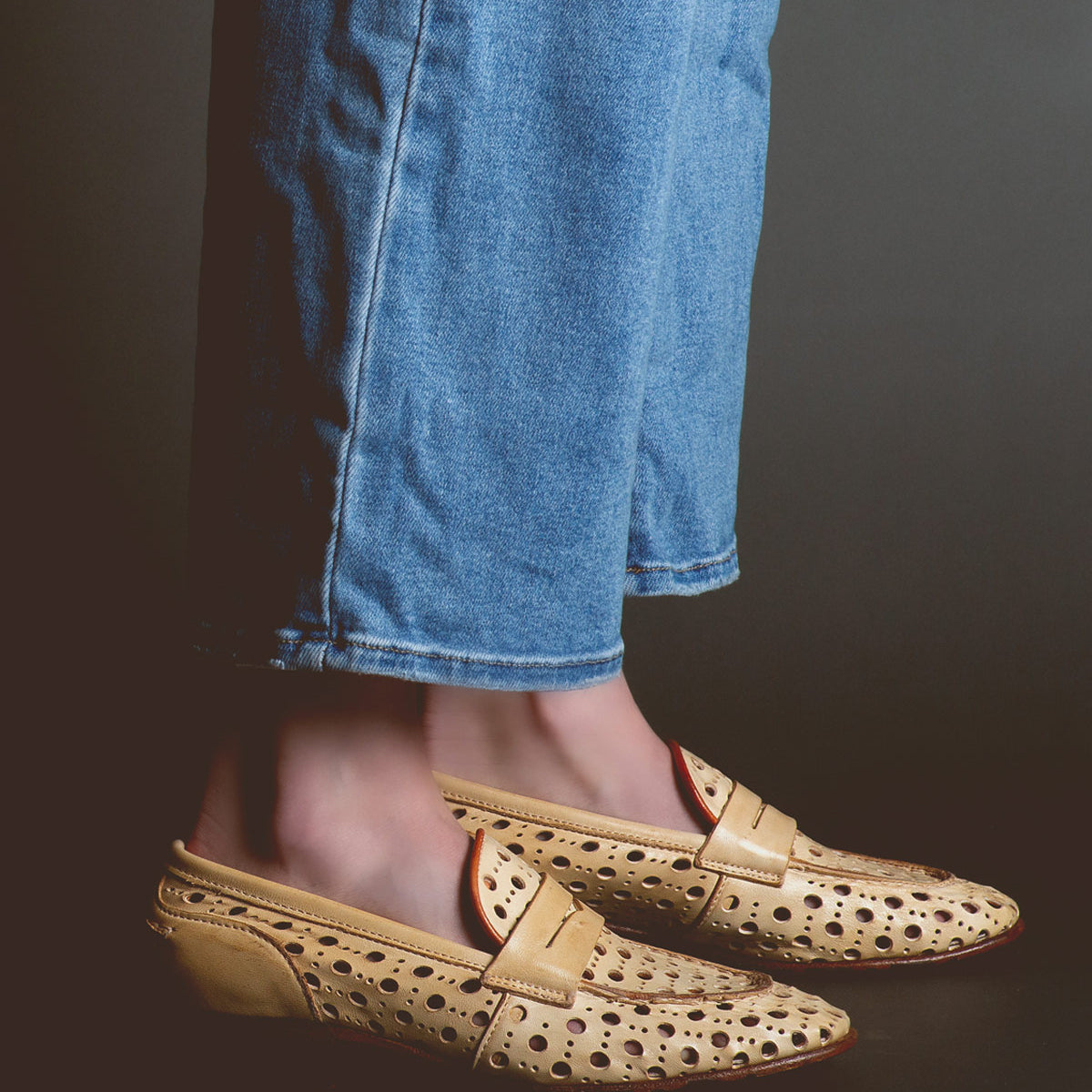 Person wearing blue jeans and tan loafers handcrafted in Italy with a playful cutout pattern called Cornflower by Bed Stu.