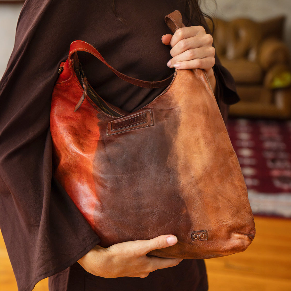 A person holds a slouchy, multicolored Bed|Stü Dallas LTC shoulder bag featuring tones of red, brown, and tan.