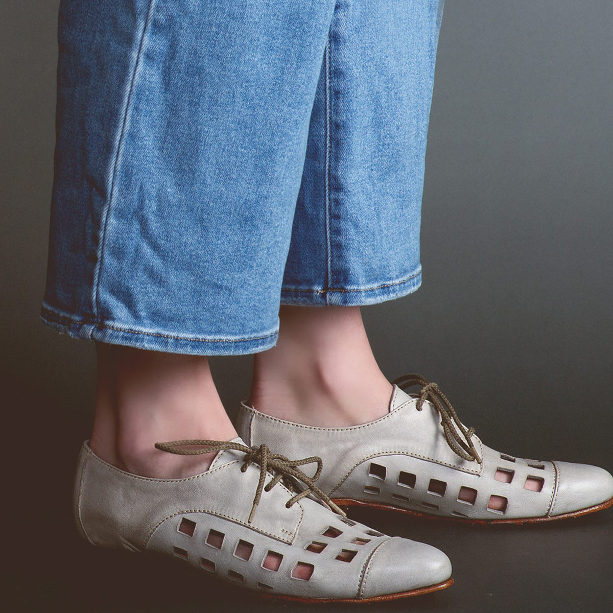 Person wearing playful Decoy lace-up derby shoes by Bed Stu, handcrafted in Italy, paired with blue denim pants against a dark background.