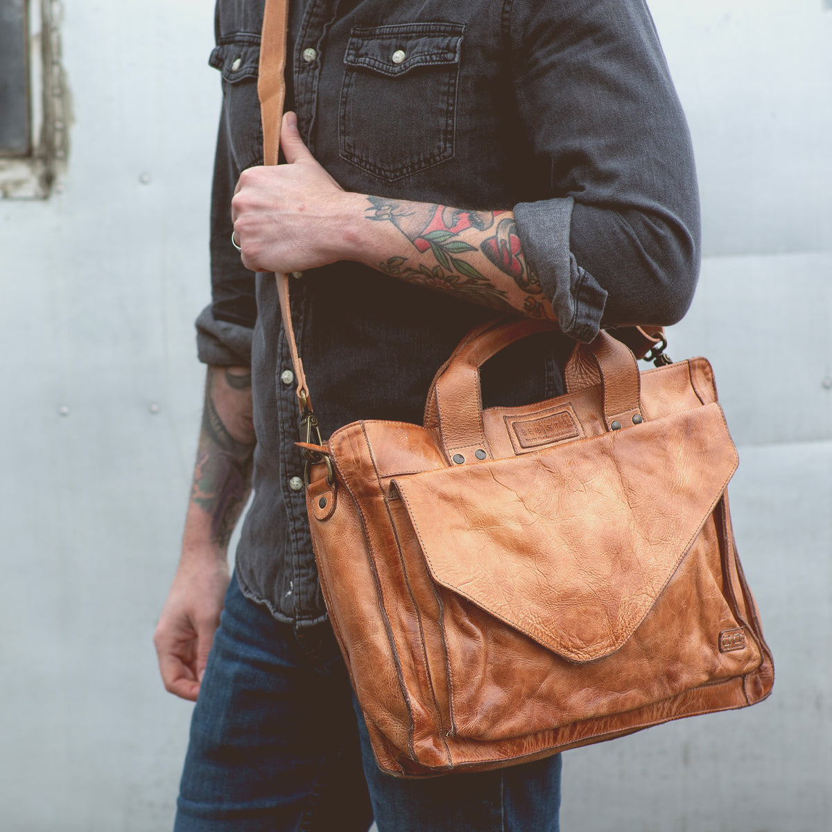 A man with tattoos holding a Bed Stu Tan leather briefcase exuding organization.