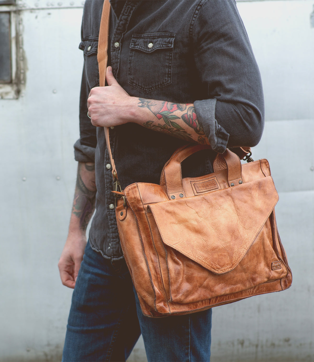 A man with tattoos holding a Bed Stu Tan leather briefcase exuding organization.