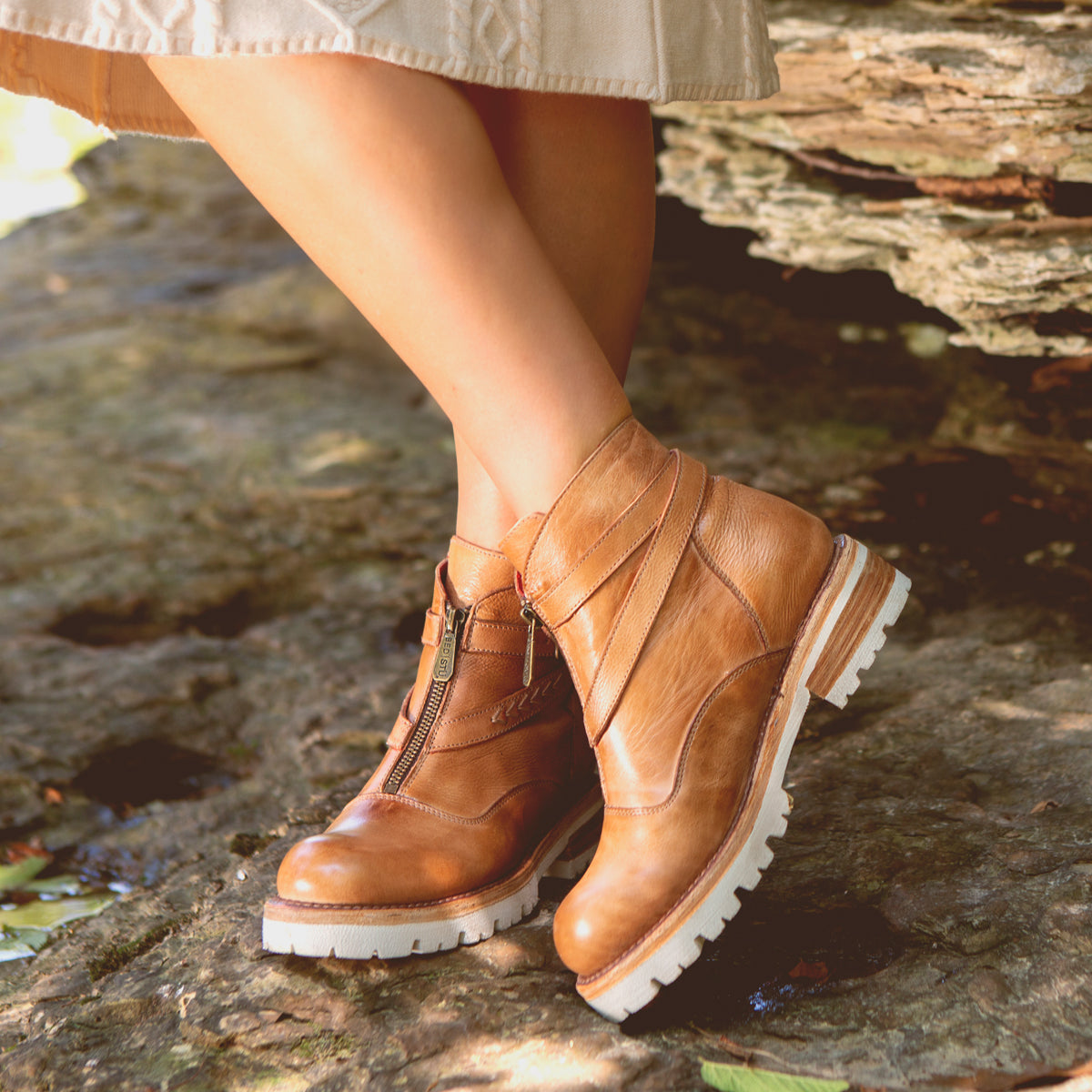A woman wearing lightweight tan leather Bed Stu Dessa ankle boots standing on a rock.