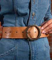 A person wearing a blue denim outfit with a modern style Bed Stu Dreampath EM genuine leather belt featuring a large octagon metal buckle.