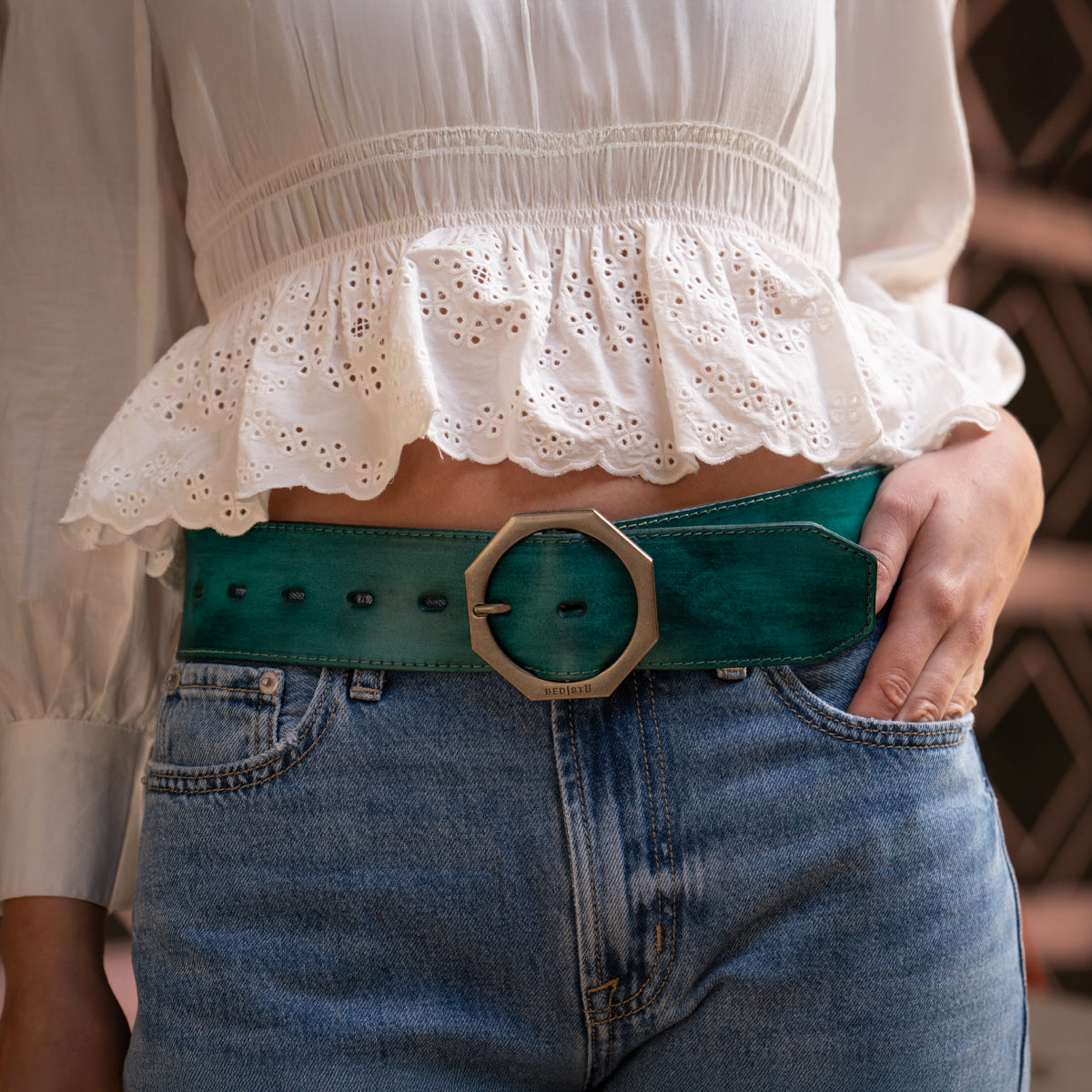 Person wearing a white ruffled blouse, blue jeans, and the Dreampath green genuine leather belt from Bed Stu featuring a large round gold buckle.