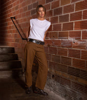 Wearing the Bed Stu "Dreampath" genuine leather belt with an octagon metal buckle, a woman in a white sleeveless shirt, brown pants, and black shoes stands by a brick wall near a staircase.
