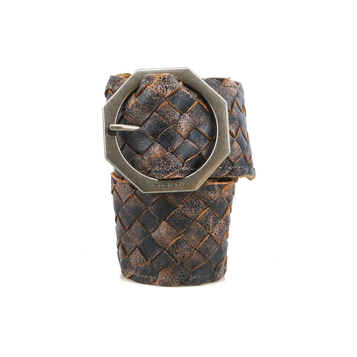 The Bed Stu Dreamweaver is a brown and black vintage boho belt, woven from leather with a large hexagonal metal buckle, shown rolled up and upright against a white background.