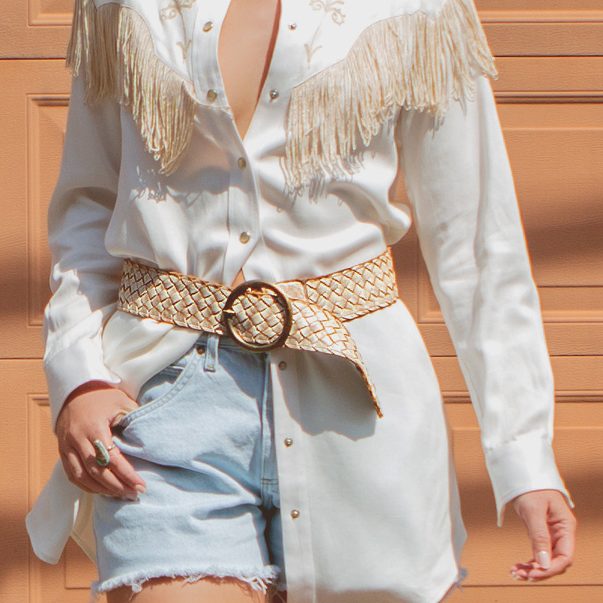 Woman wearing a white fringed Dreamweaver shirt, a distressed leather Belt Stu belt, and denim shorts.