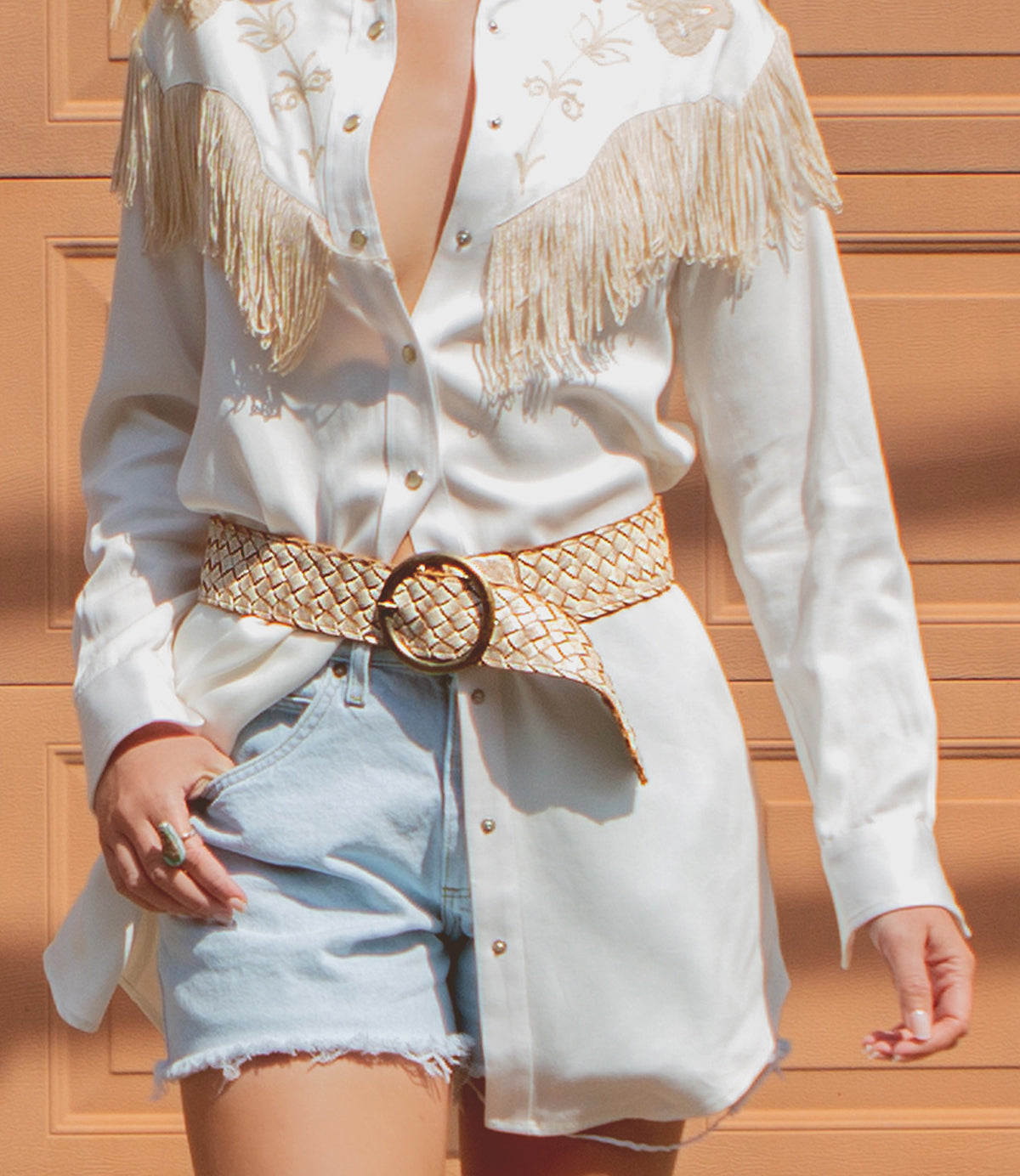 Woman wearing a white fringed Dreamweaver shirt, a distressed leather Belt Stu belt, and denim shorts.