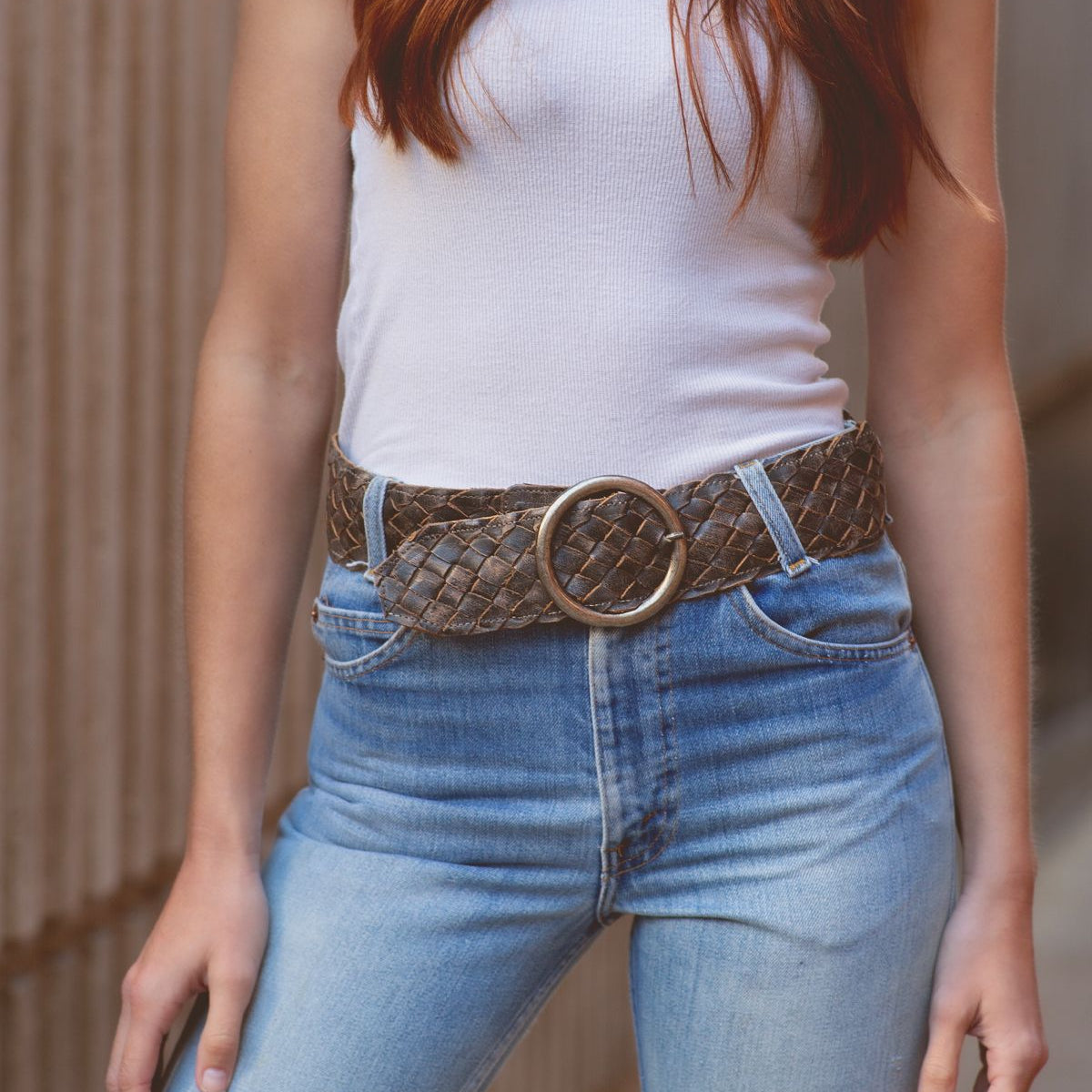 A person wearing the "Dreamweaver" white sleeveless top and high-waisted jeans from Bed Stu, along with a woven belt featuring a brass-tone buckle, stands against a neutral background, exuding a touch of vintage allure.