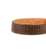 The Bed Stu Dreamweaver is a round, shallow basket of tightly woven brown strips and a smooth, flat tan interior—perfect for adding vintage boho charm to any room. No visible handles.