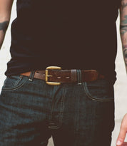 A person wearing a black shirt and dark blue jeans with a dapper appeal, highlighted by the Drifter belt from Bed Stu—a perfect weekend accessory.