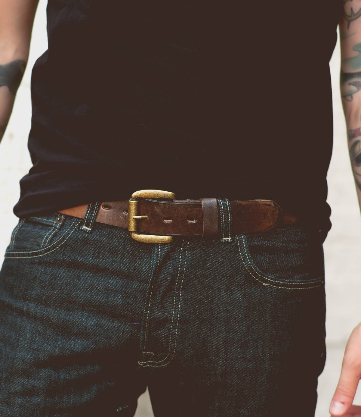 A person wearing a black shirt and dark blue jeans with a dapper appeal, highlighted by the Drifter belt from Bed Stu—a perfect weekend accessory.