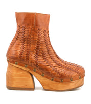 The Ellasphin by Bed Stu is a brown leather ankle boot featuring woven detailing, a thick wooden heel, platform sole, and brass studs—artisan footwear with timeless sculptural style.