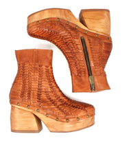 Two Bed Stu "Ellasphin" boots are displayed side by side on a white background—brown handwoven platform footwear with wooden soles, brass studs, and side zippers, showcasing unique artisan sculptural style.