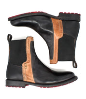 The Bed Stu Ethic boots are black Chelsea boots with brown accents, made from vegetable-tanned leather. They feature black elastic side panels, red Vibram soles, and pull tabs at the back, shown side by side.