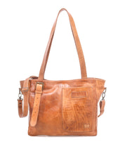 The Bed Stu Explicit LTC is a light brown seasoned leather bag with two top handles, an adjustable strap, and a front patch pocket with stitched details plus a small embossed logo, adding rustic appeal.