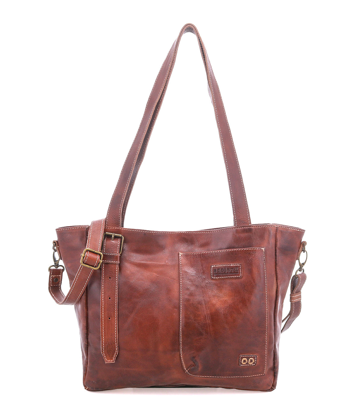 The Bed Stu Explicit LTC is a brown leather shoulder bag with two handles, an adjustable strap, visible stitching, a front pocket, and a small rectangular logo patch for rustic appeal and versatile utility.