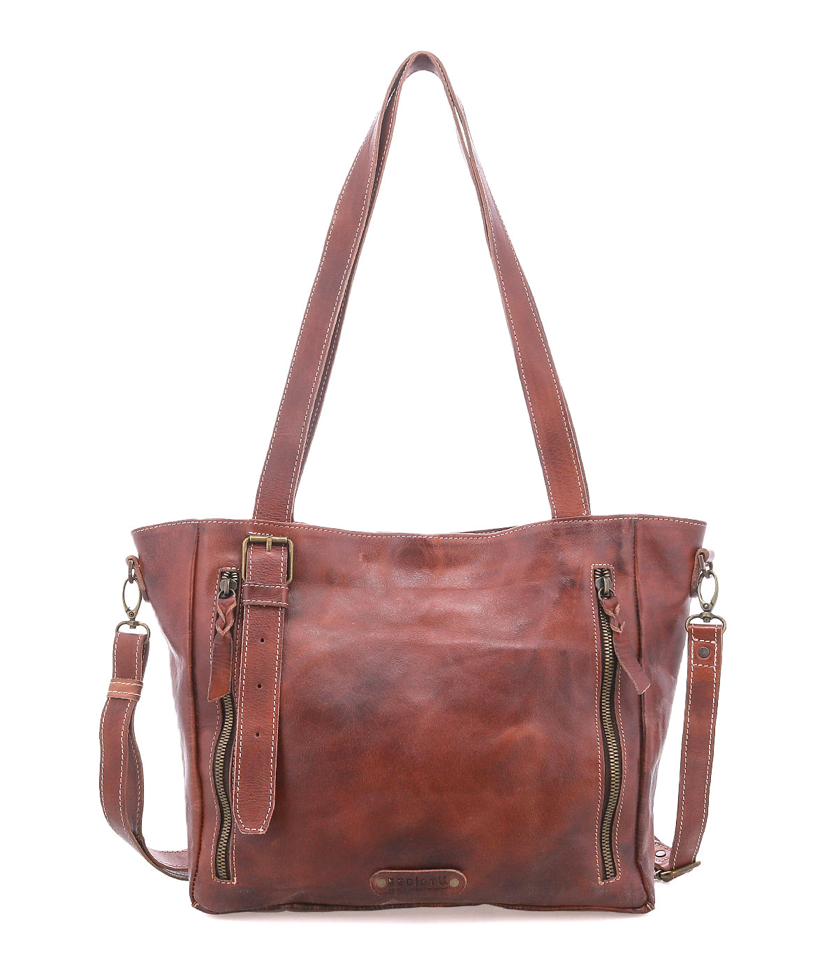 The Bed Stu Explicit LTC is a rustic brown leather tote bag with two top handles, front zippered pockets, and a detachable shoulder strap, shown against a white background.