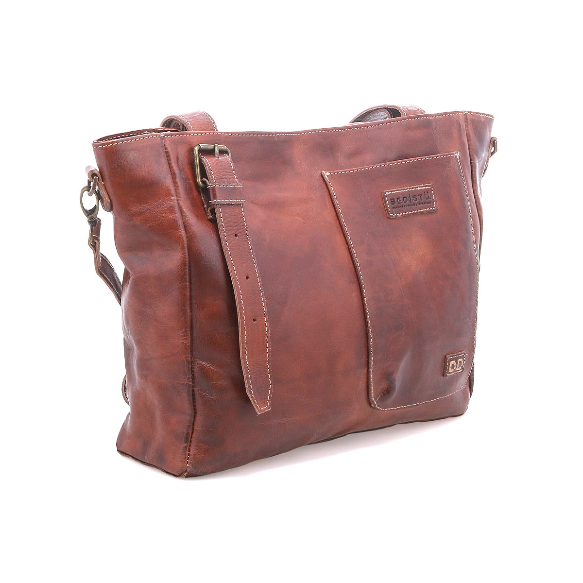 The Bed Stu Explicit LTC is a brown leather rustic bag with a front pocket, adjustable strap, and visible stitching, shown against a white background.