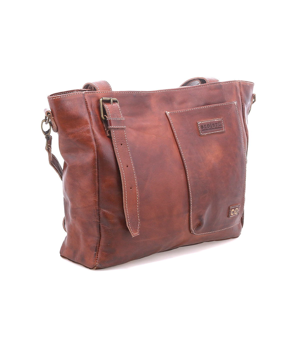The Bed Stu Explicit LTC is a brown leather rustic bag with a front pocket, adjustable strap, and visible stitching, shown against a white background.