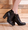 A woman wearing the Bed Stu Isla black leather ankle boots on a wooden floor.