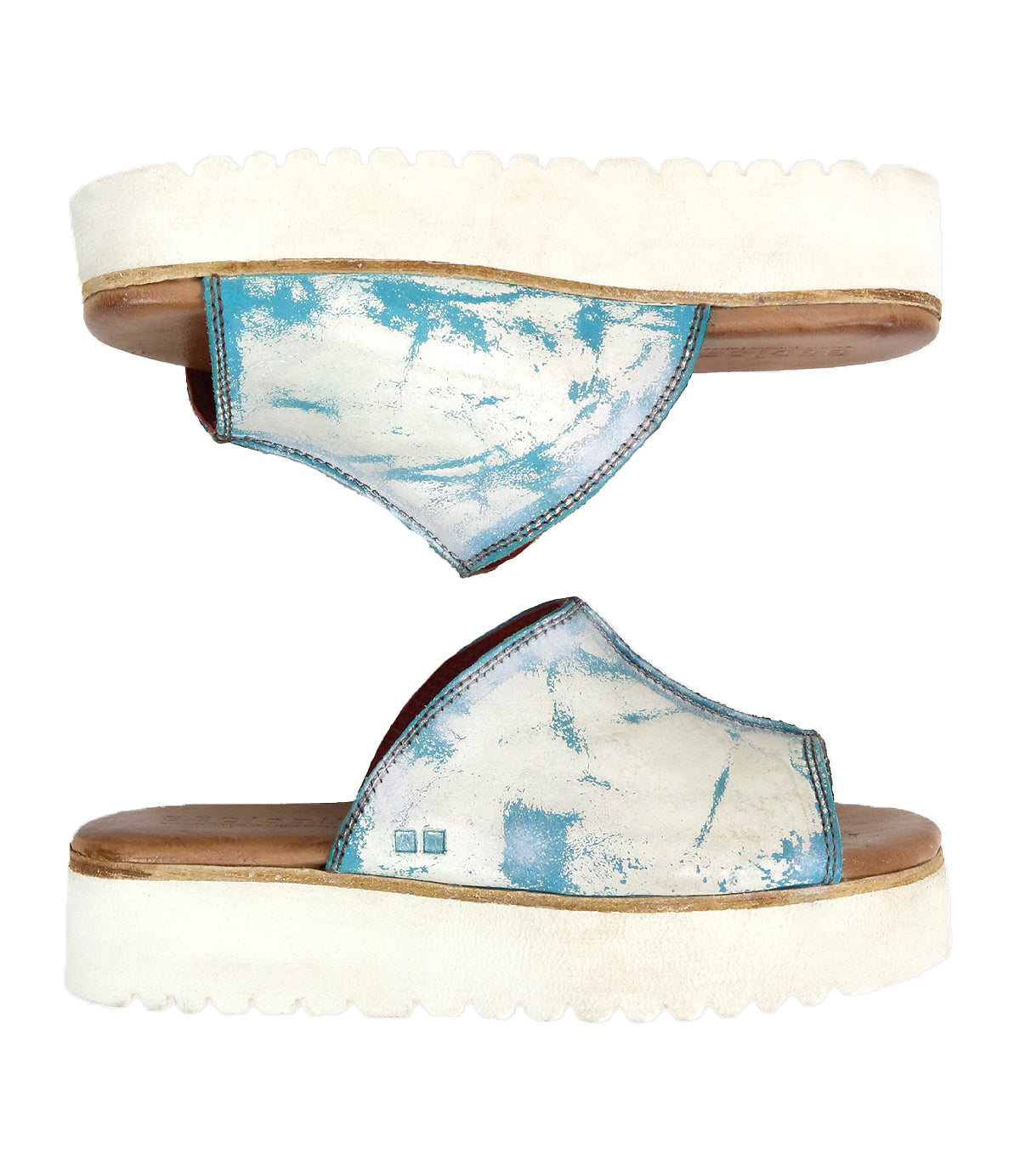 The Bed Stu Fairlee II features two white flatform slide sandals with blue tie-dye patterns, open toes, and a leather-lined footbed for added comfort, shown from the side and above.