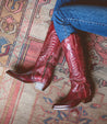 A woman wearing a pair of red leather Bed Stu Finito cowboy boots on a rug.