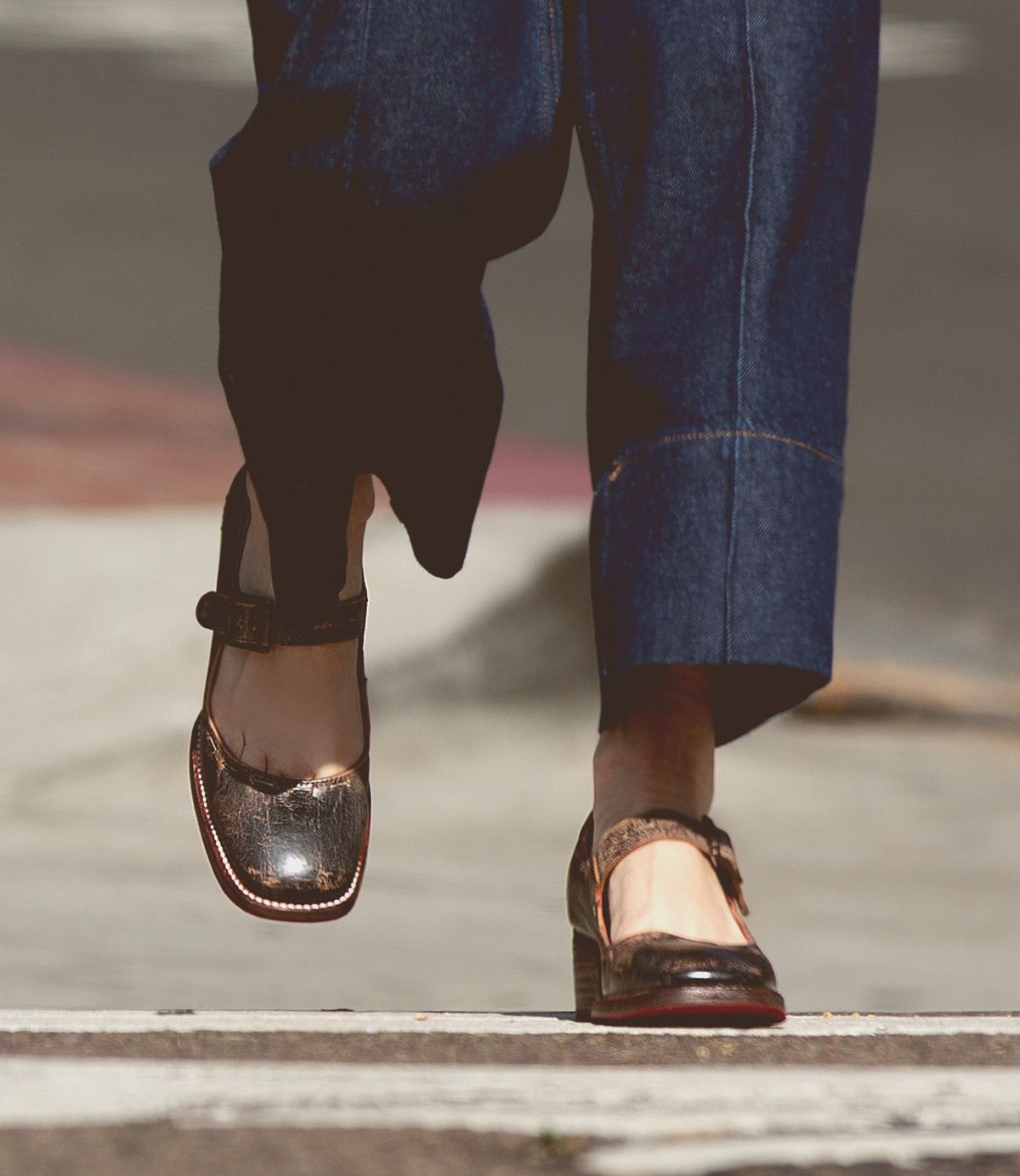 Person wearing Bed Stu's Forefront leather Mary Jane shoes with a comfortable heel and wide-leg denim pants, walking across the pedestrian crossing.
