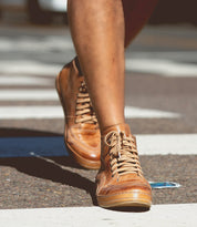 Close-up of a person walking on a city street wearing the Bed Stu Formation high-top sneakers in tan leather with a modern design.