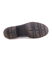 The underside of a worn black shoe sole with visible tread patterns and textured surface reveals the durability of Goodyear welted craftsmanship, echoing the rugged style of moto-inspired men’s leather boots, characteristic of Bed Stu's "Fellow" design.