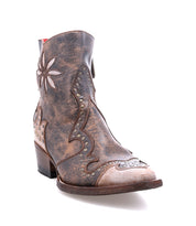 The Bed Stu Frio is a brown distressed leather Western bootie featuring decorative stitching, floral cutouts, and antiqued brass studs accenting a floral ankle design, shown on a white background.