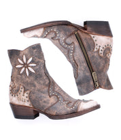 The Bed Stu Frio is a brown distressed leather Western bootie with floral cutouts, antiqued brass studs, and side zippers, displayed on a white background.