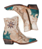 The Bed Stu Frio is an ankle-height, distressed tan leather Western bootie with turquoise accents, floral cutouts, brass studs, decorative stitching, side zippers, and wooden heels—shown on a white background.