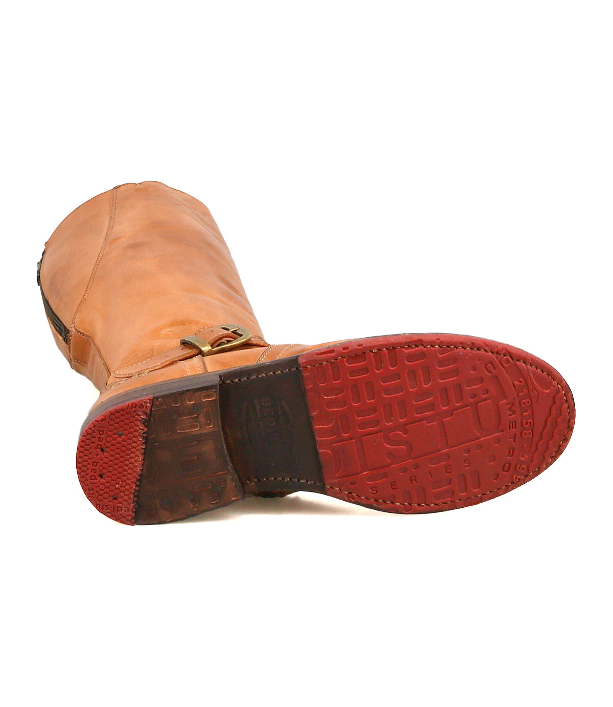 The Bed Stu Glaye boot, crafted in tan leather, rests on its side to reveal a red rubber sole with textured treads and a vintage buckle accent near the ankle.