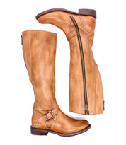 Two tan leather Bed|Stü Glaye Wide Calf equestrian boots, one upright and one horizontal, featuring full-length side zippers and ankle straps with buckles.