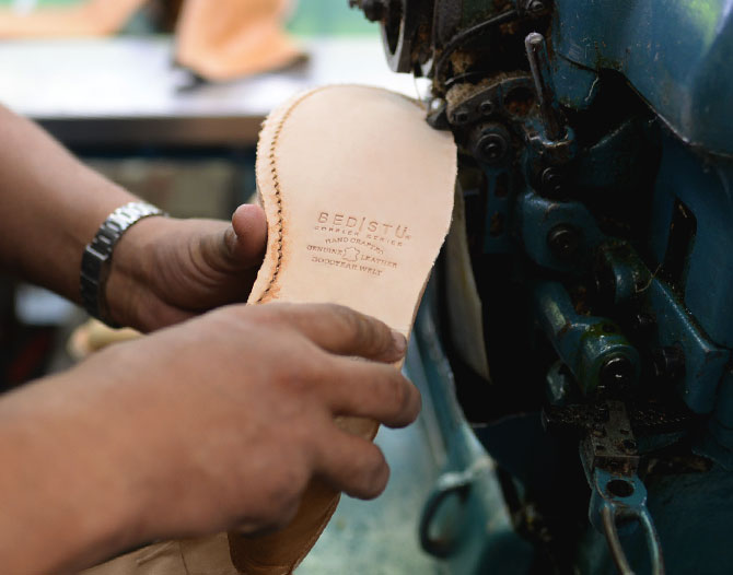 Man's hands holding unfinished shoe stitching on the Goodyear Welt to the bottom. 
