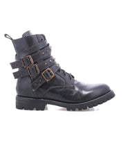 The Bed Stu Grab is a black leather combat-inspired boot with studded buckle straps and metal studs, shown in side profile on a white background. It features a sturdy Vibram rubber lug sole for traction and durability.