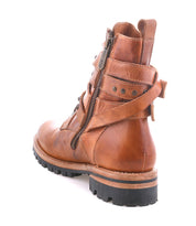 The Bed Stu Grab is a brown leather combat-inspired ankle boot with Vibram lug sole, side zipper, studded buckle straps, and metal studs, shown from the back and side on a white background.