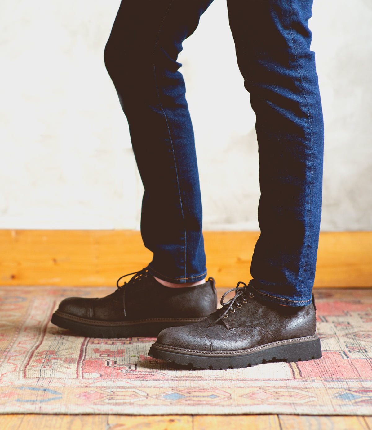 A man wearing jeans and a pair of Bed Stu Grant, standing on a rug.